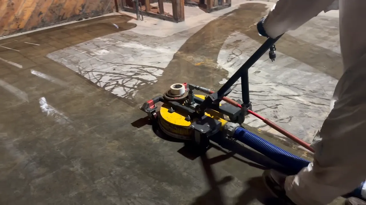 Clean concrete swaths beside dark floor adhesive not yet removed, during asbestos flooring removal with water