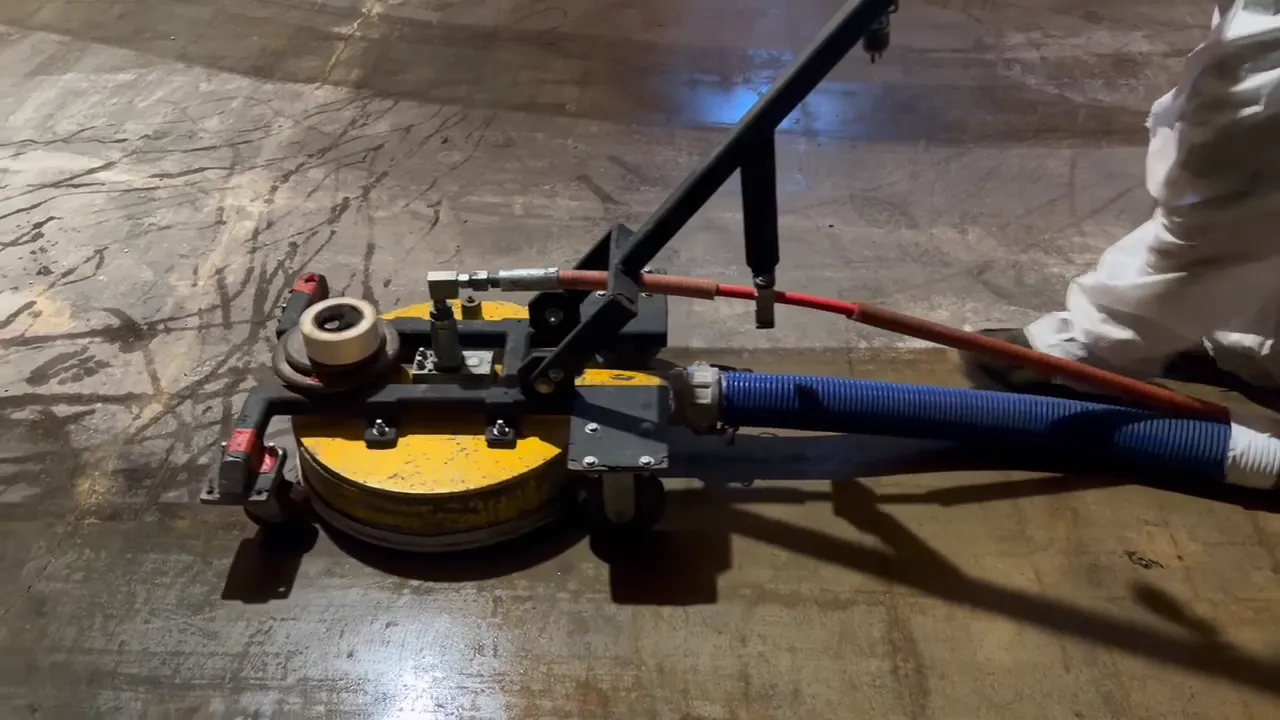 UHP water blasting head and blue vacuum recovery hose working across a slab during asbestos mastic removal