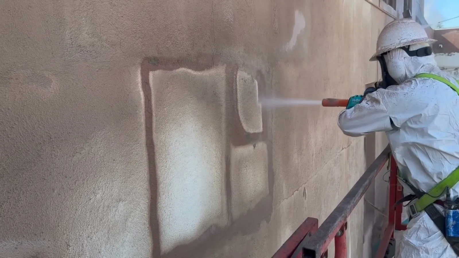Worker on a lift slurry blasting an exterior stucco wall to bare substrate